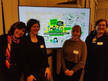 Vier Frauen des Projkets JAzA stehen vor einem Grafic Recording des Fachtags. 