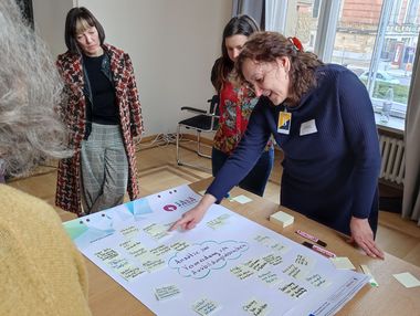 Die Projektleiterin Birgit Voigt zeigt auf ein Post-It, das auf ein Plakat geklebt wurde. Thema des Plakats: Vermeidung von Ausbildungsabbrüchen.