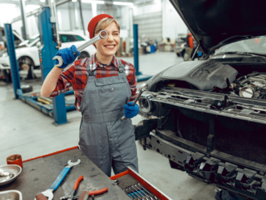 Fröhliche junge Mechanikerin mit Spaß bei der Arbeit, die zwei Schraubenschlüssel in der Hand hält.